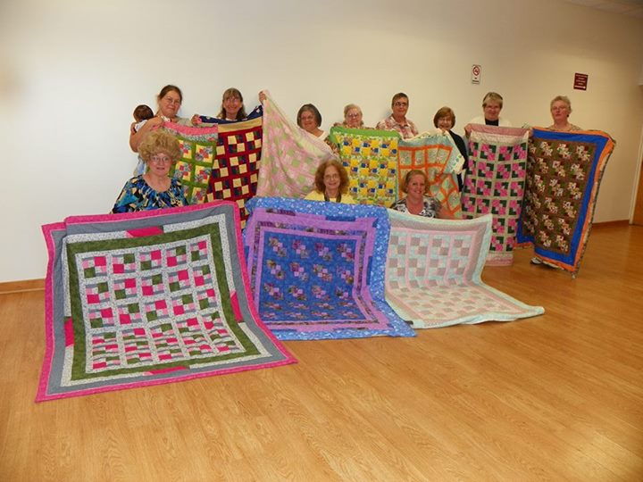 ten quilters holding their colorful quilts